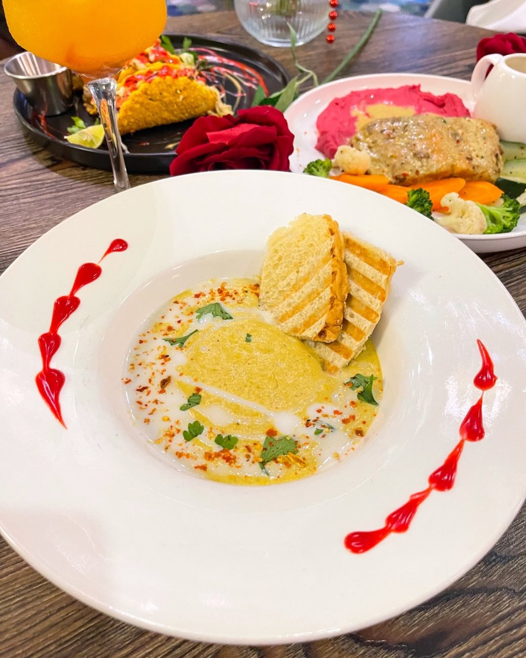 A table set with roses, a creamy soup with grilled bread and cocktails