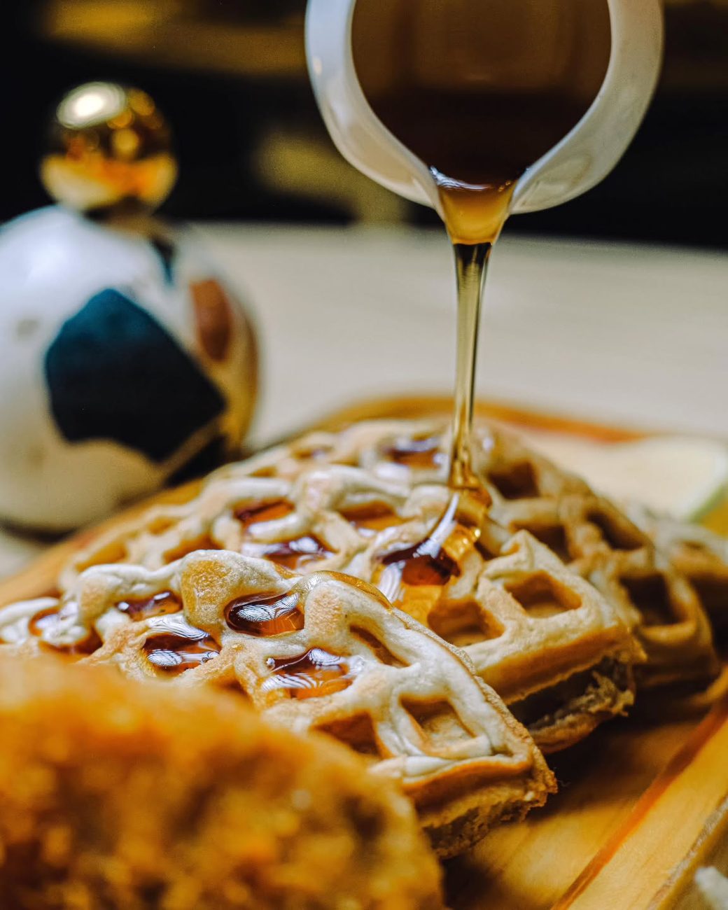 Maple syrup pouring over waffles served with crispy chicken